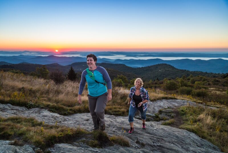 Two women hiking up a mountain with sunset and mountains in background
