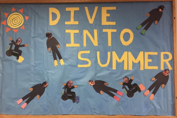 Dive-Into A bulletin board says Dive Into Summer and features little divers with students' faces on them.