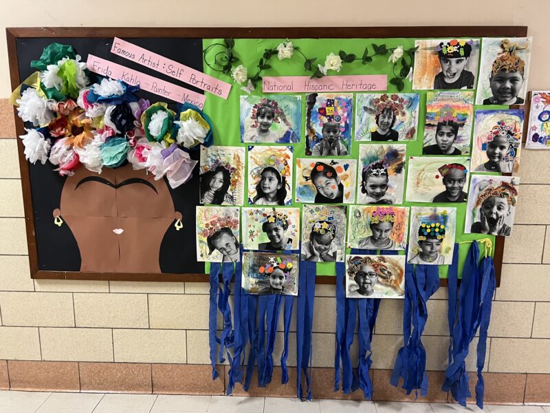 Hispanic-Heritag-Susan-Stierlen A bulletin board features a head with flowers on it and pictures of all the students in the class. It says Famous Artists Frida Kahlo.