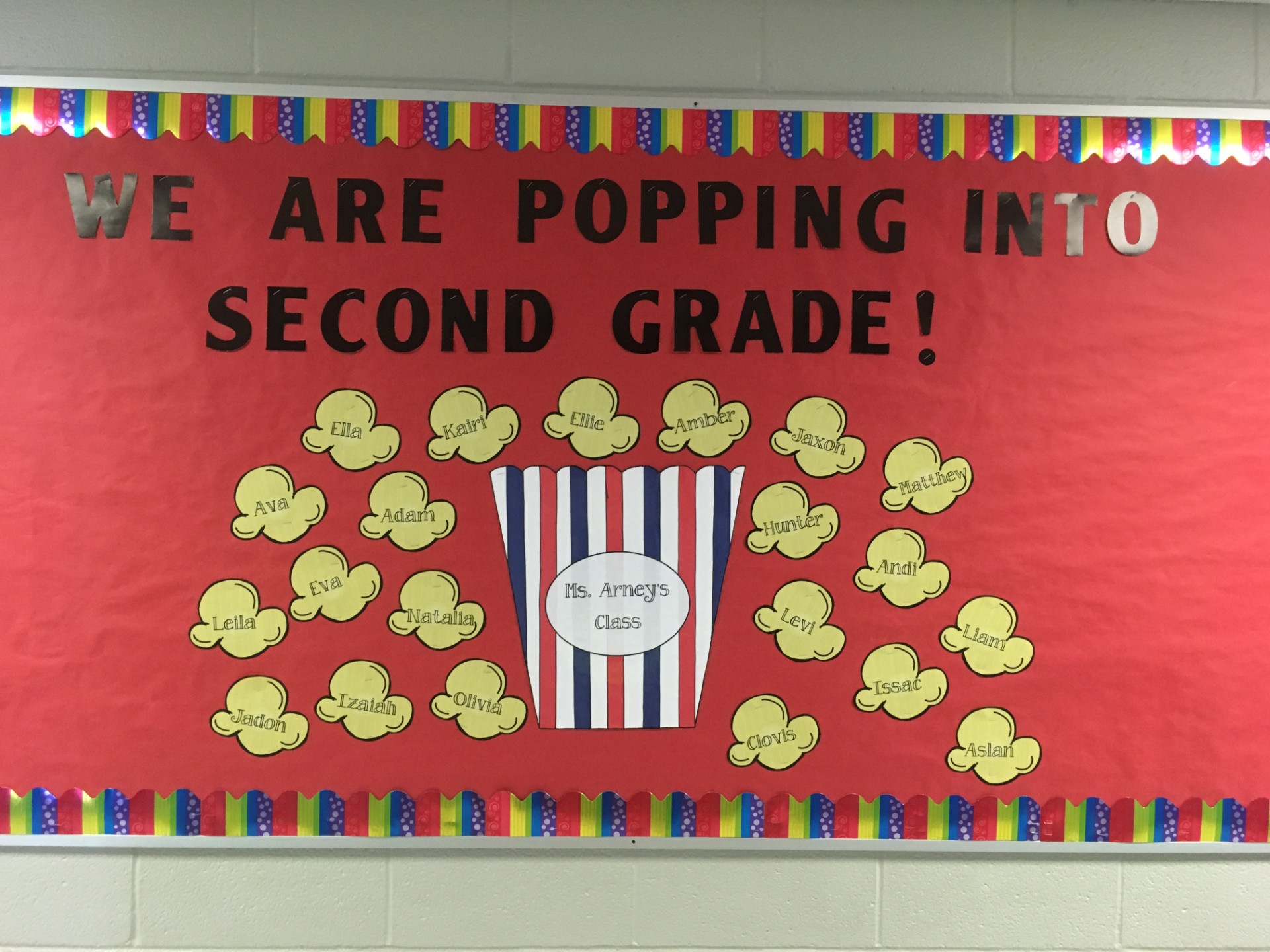 Poppin A bulletin board says We Are Popping Into Second Grade. Popcorn kernels have students' names on them.