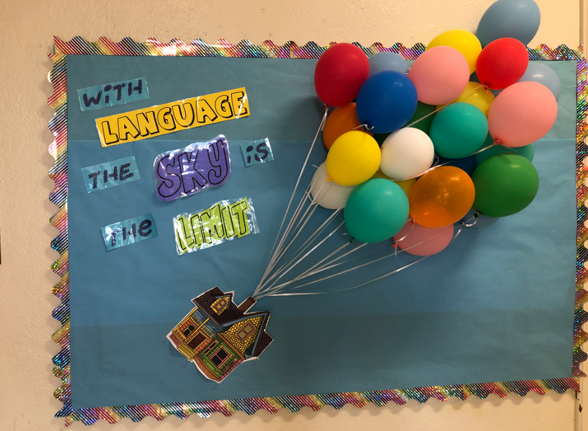 Up-House A bulletin board has a small house on it that looks like it is being carried away by a bouquet of actual blown up balloons.
