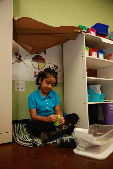 First Grade Calm-Down Spot – Childhood Trauma Was Hiding at This School First grade girl sitting on floor using a squeeze noodle.
