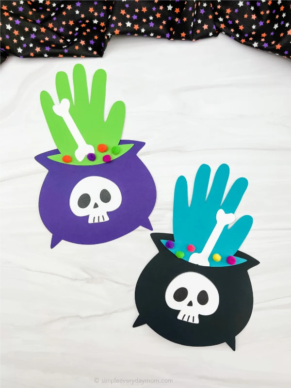 handprint-witchs-cauldron WItch's cauldron paper craft with a black pot embellished by a skull and a traced handprint sticking out as the smoke as an example of halloween crafts for kids