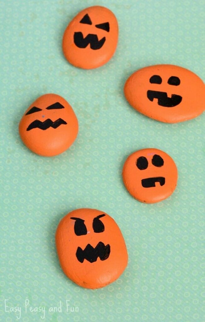 halloween-rock-painting Several rocks are painted orange with black jack o' lantern faces painted on them