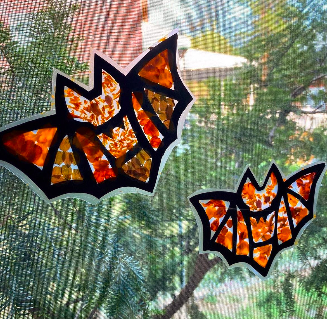 suncatcher-bats A black-outlined bat shape is filled in with splotchy orange paint as an example of halloween crafts for kids