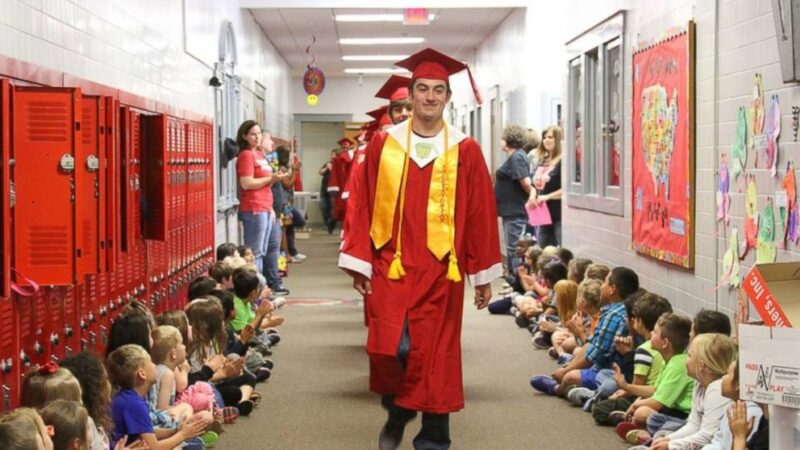 graduation-walk High school seniors in graduation gowns parade down a school hallway lined with elementary students