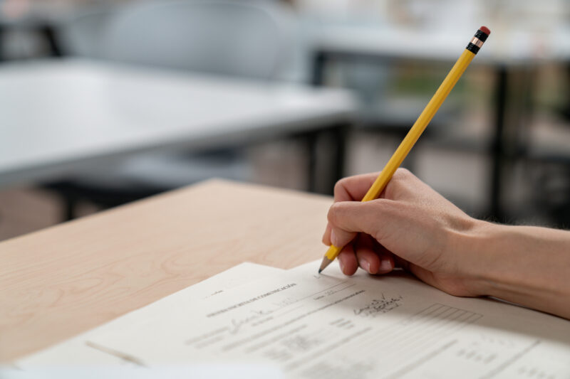 Close-up on a university teacher grading an exam student hand holding a pencil taking a test