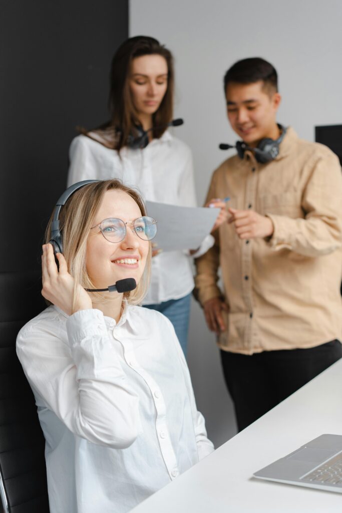 Two figures are in the background wearing headphones. A woman with a headset with a microphone is in the forefront in this example of music careers.