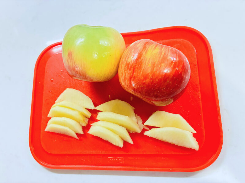 an image of two apples and apple slides on a red cutting board