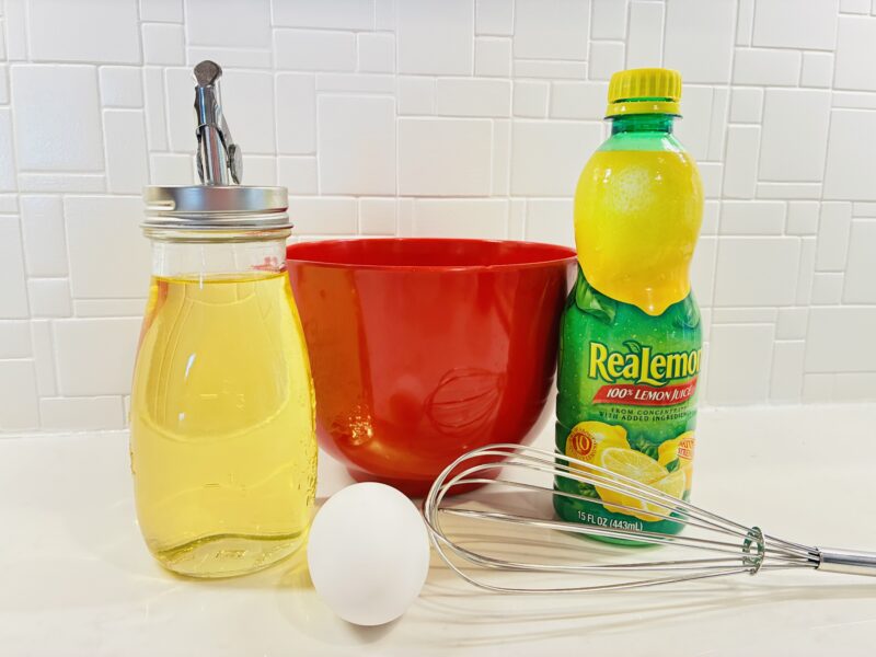 oil, a red bowl, an egg, a whisk, and lemon juice
