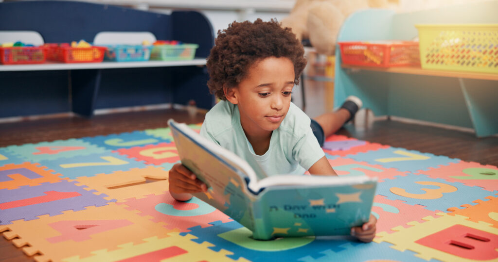 Boy, book and floor in classroom for development, storytelling and knowledge at academy. Child, learning and study on mat for scholarship, reading and info with course at elementary school